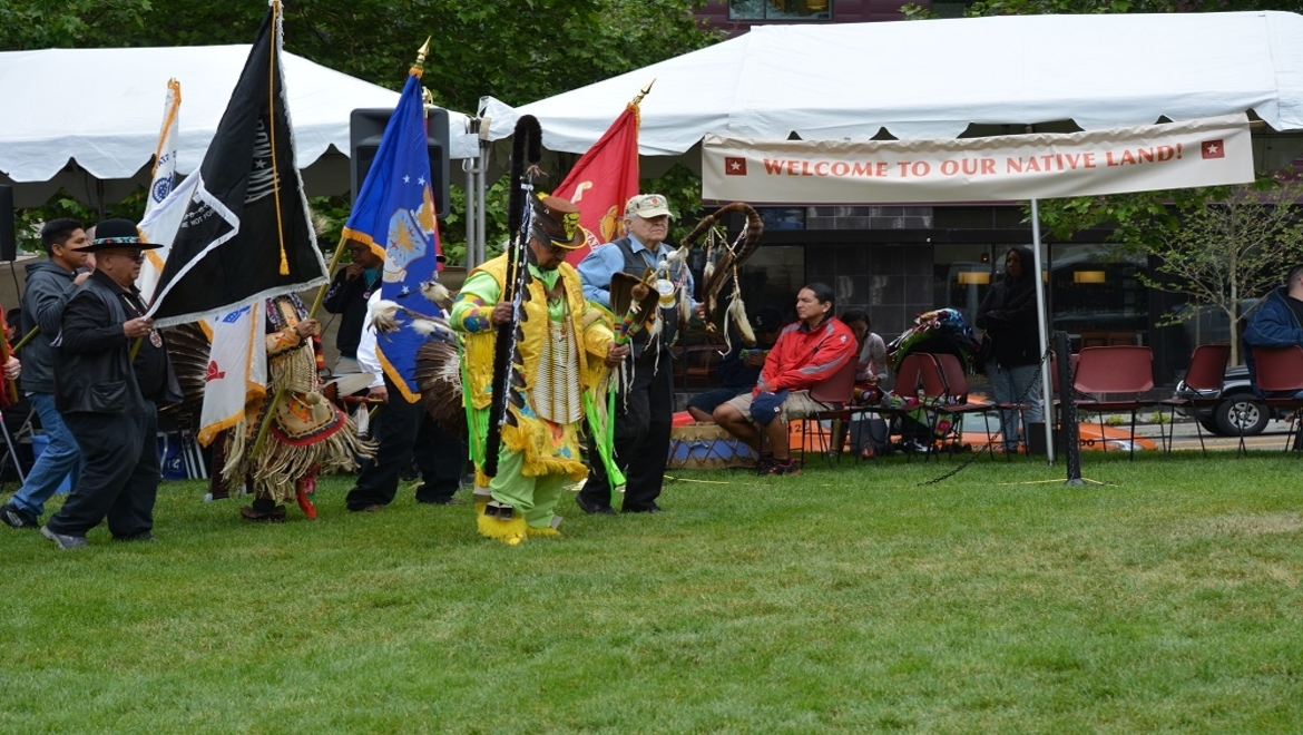 Native American celebration with traditional dress, flags and dancing